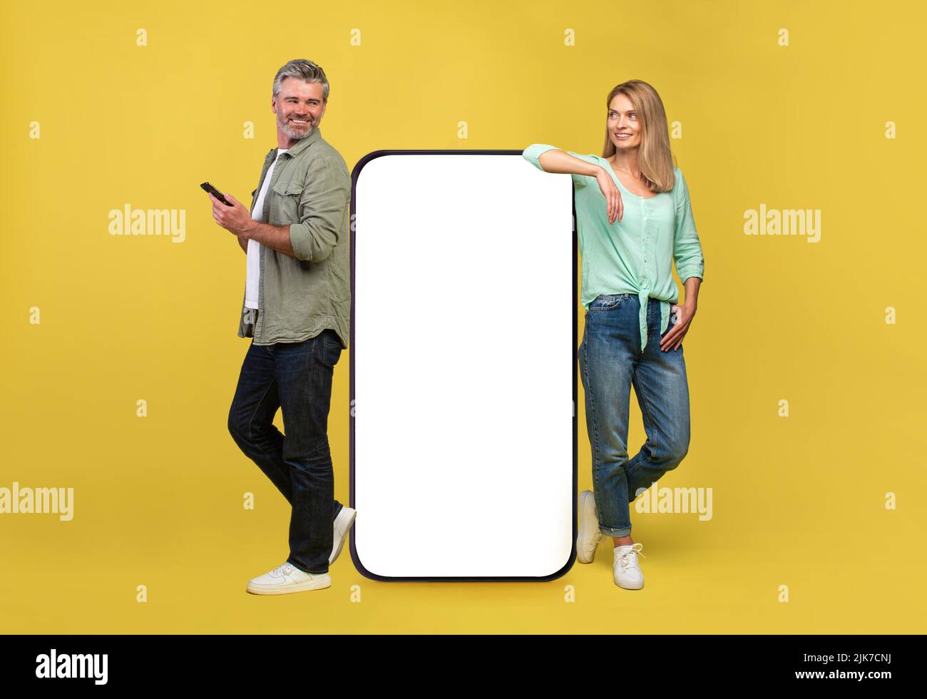 Great app. Full body length of middle aged couple leaning on big smartphone with white empty screen Stock Photo