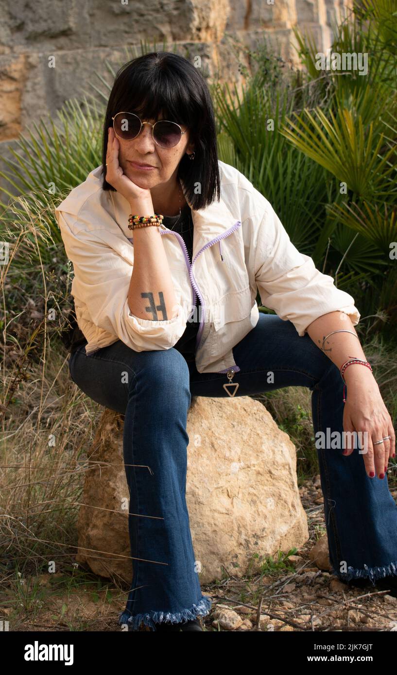 Carefree woman in casual attire sit down on a rock look at the camera Stock Photo