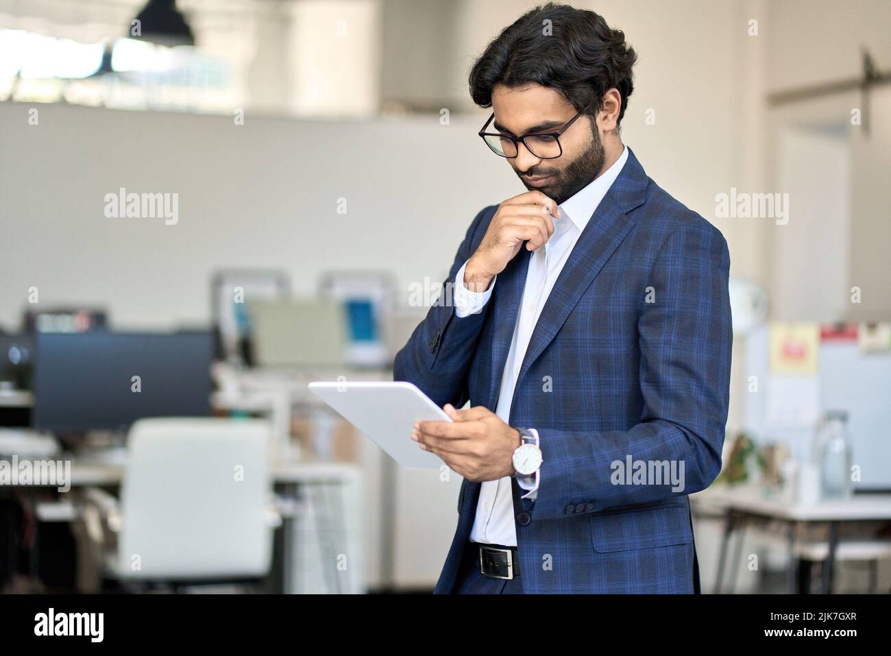 Busy indian young business man executive wearing suit using digital tablet. Stock Photo