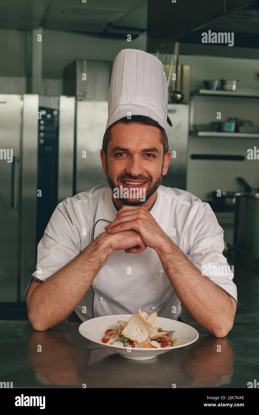 Portrait of smiling chef in uniform with cesar salat on modern kitchen ...