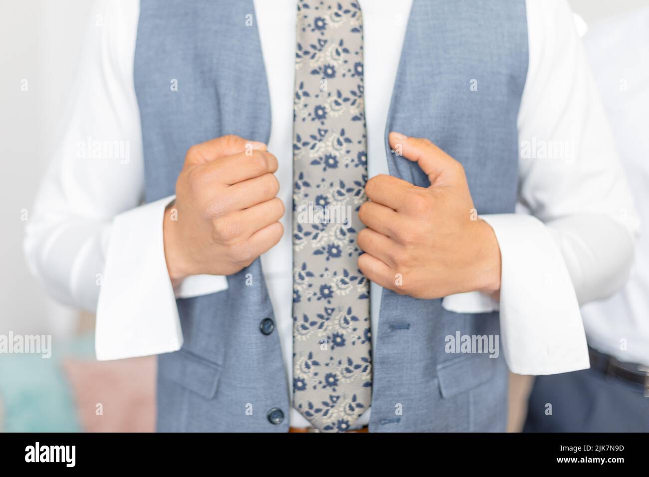 Cropped photo of man groom fiance wearing blue stylish vest, white shirt, grey tie with floral pattern unbuttoning vest. Stock Photo
