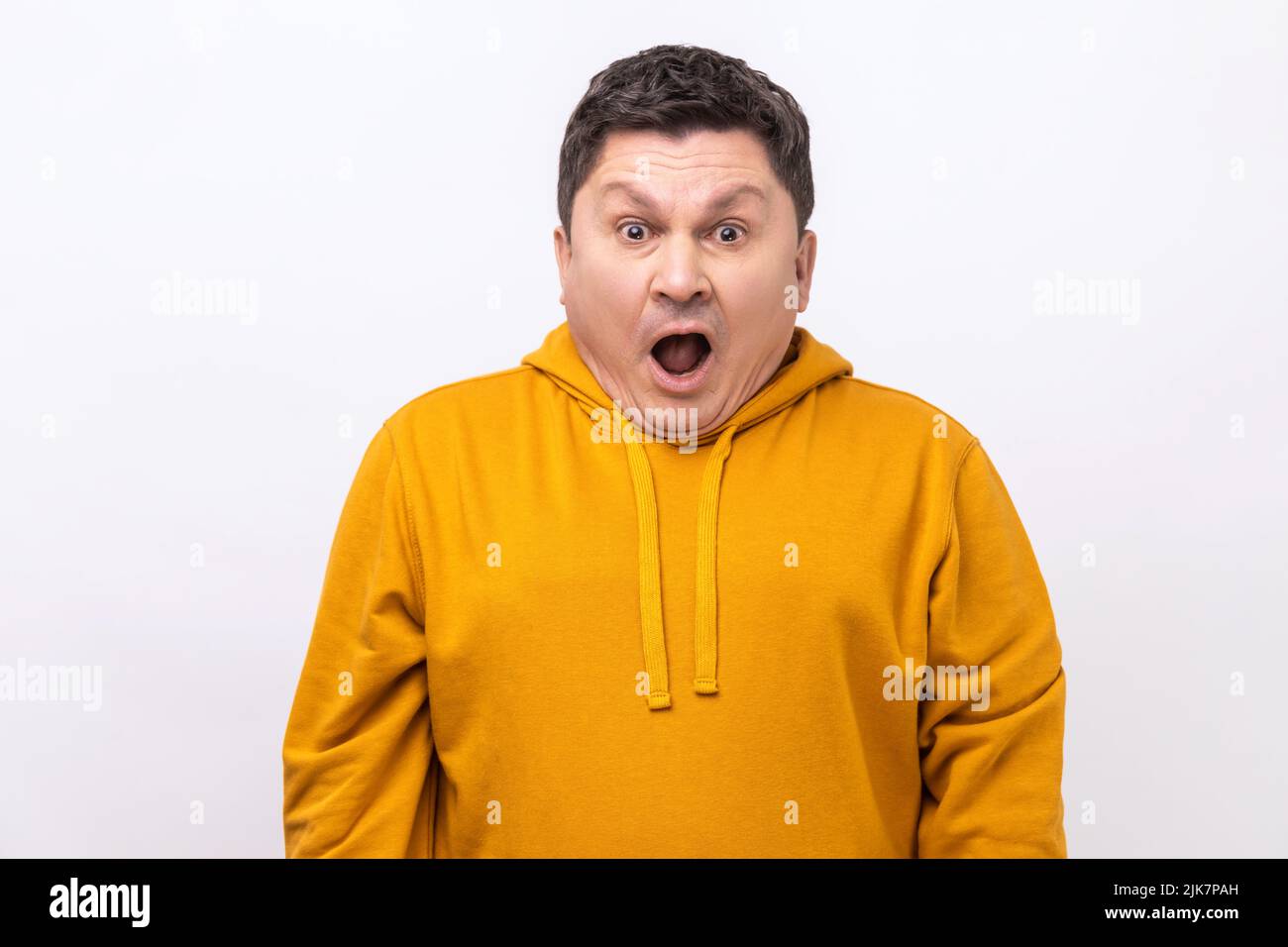 Portrait of excited man with open mouth and big amazed eyes, looking surprised and silly at camera, wondered expression, wearing urban style hoodie. Indoor studio shot isolated on white background. Stock Photo