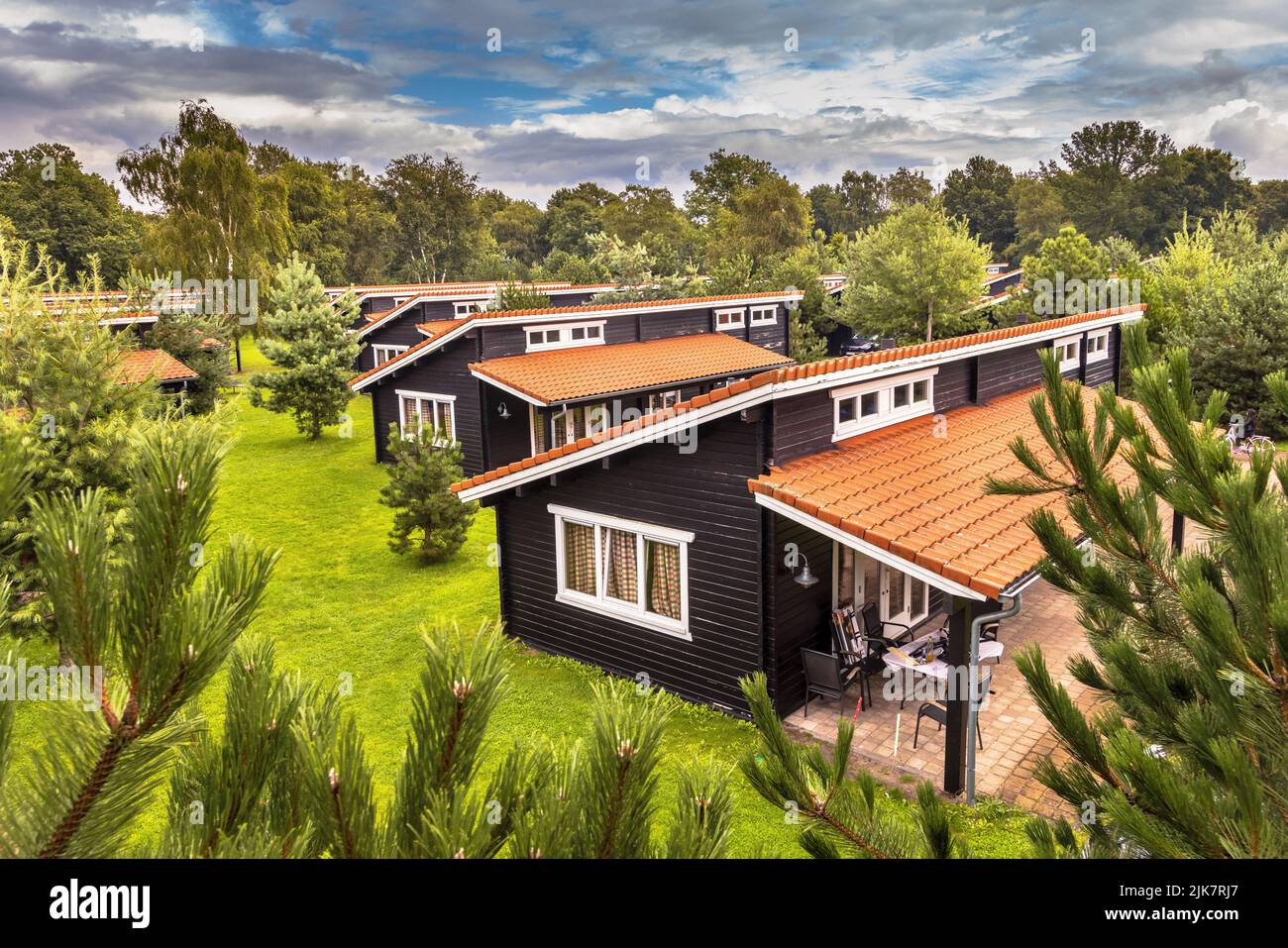 Holiday Bungalow park with identical cottages in symetrical order in green forested area. Wooden chalets with orange roof tiles in grass and bushes. N Stock Photo