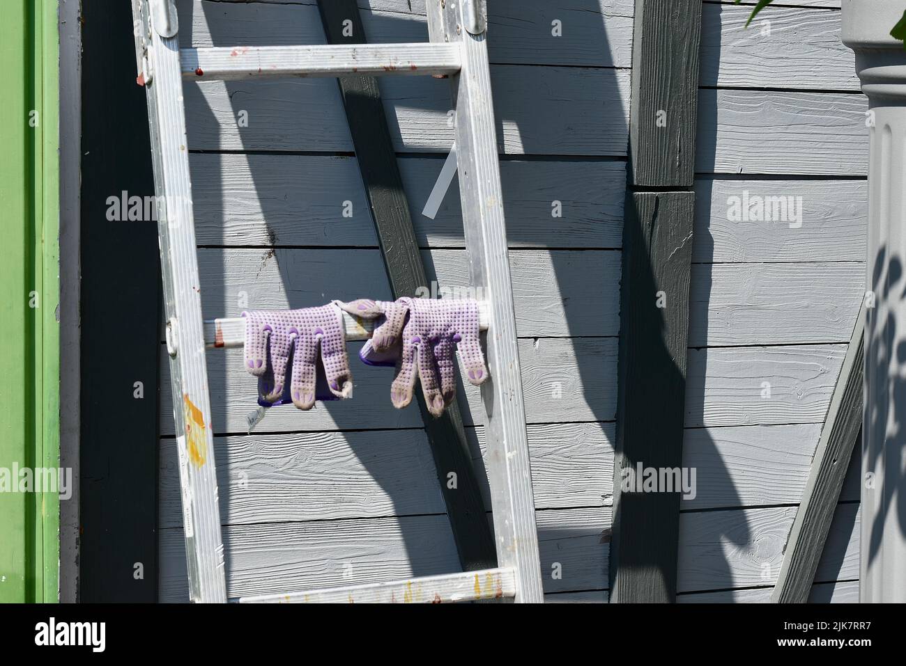 hand shoes on a ladder, shadow casting on a grey wooden door, background in the garden Stock Photo