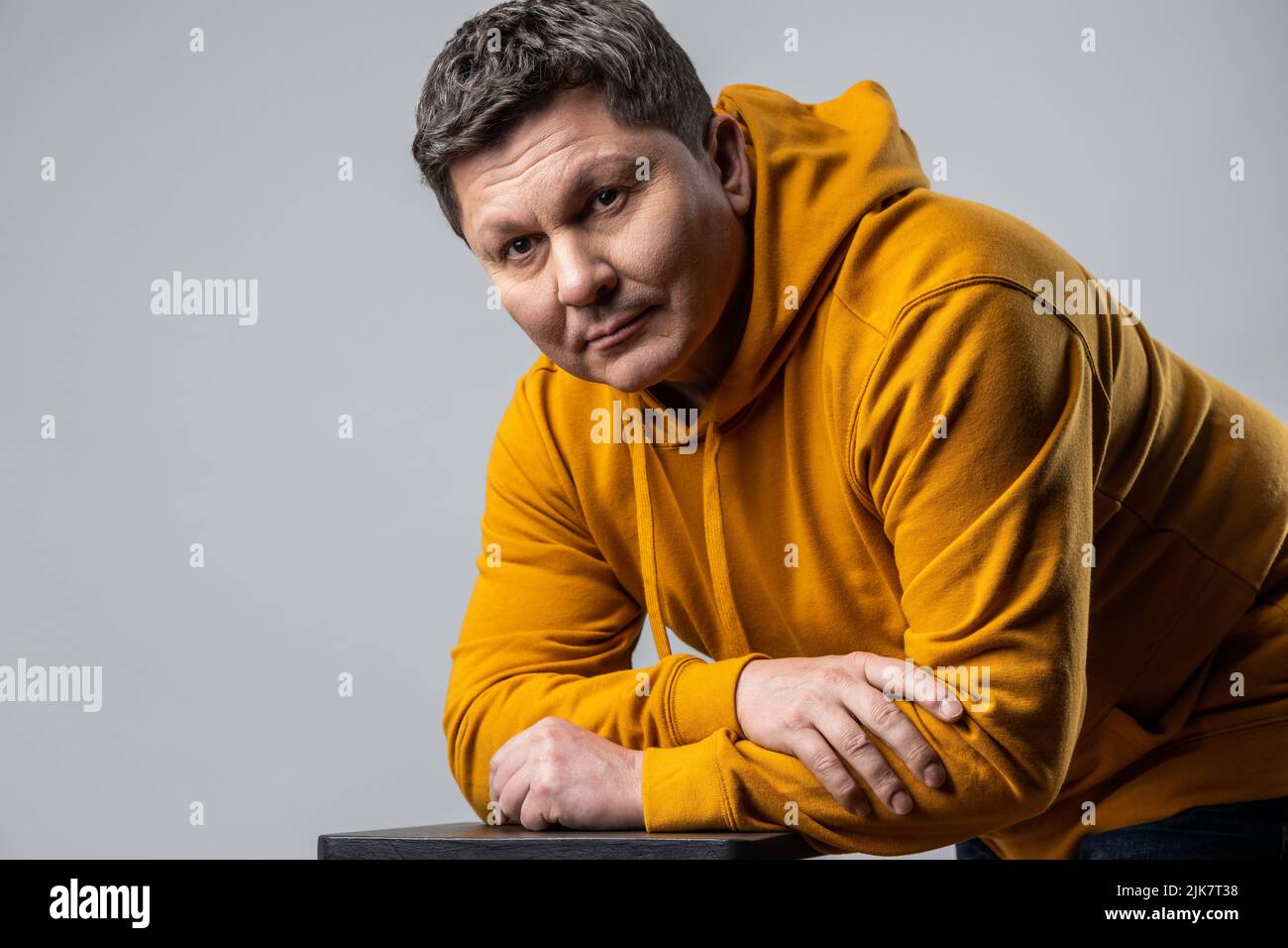 Calm attractive middle aged man looking at camera with thoughtful look, beauty, fashion portrait, wearing urban style hoodie. Indoor studio shot isolated on gray background. Stock Photo