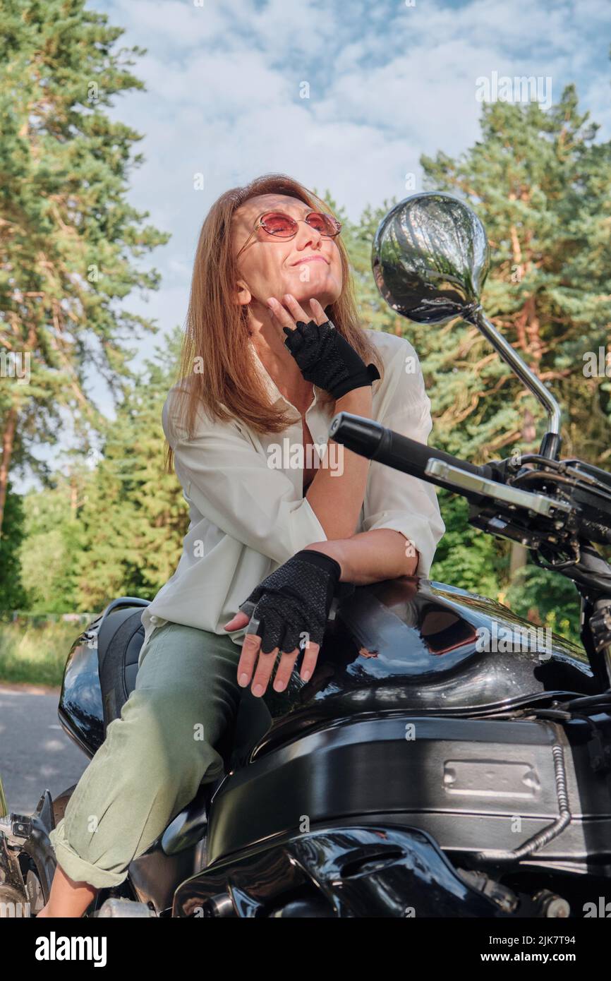 Middle age woman biker drives a motorcycle on a forest road, travels alone Stock Photo