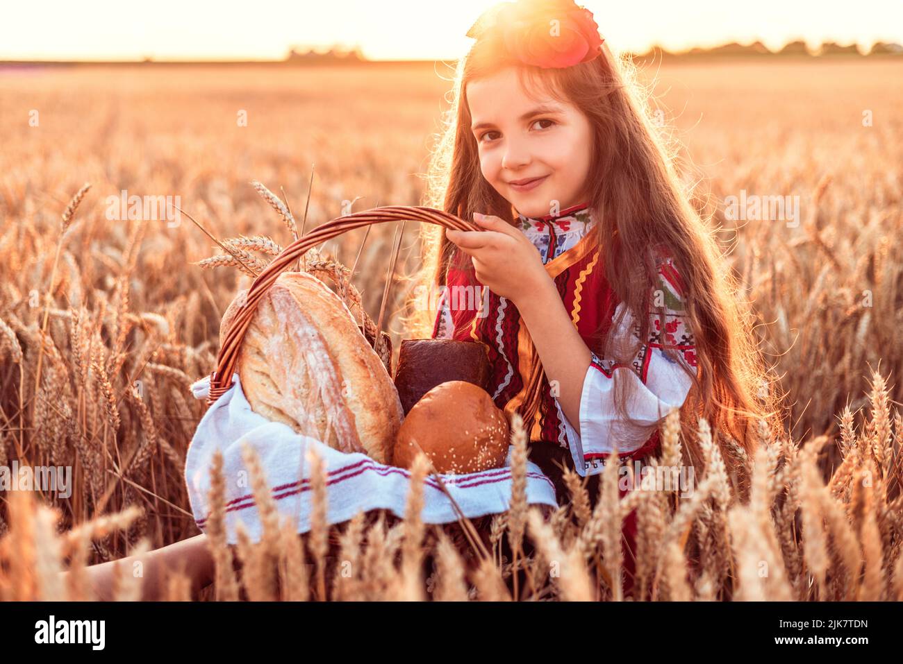 Bulgarian woman  or young girl in traditional folklore dress holds in hands golden wheat and freshly baked homemade bread in a bag Stock Photo