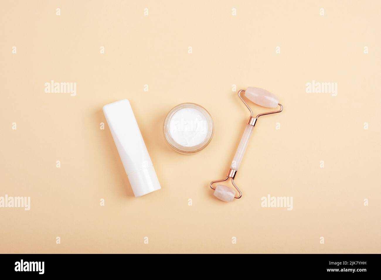 Rose quartz crystal facial roller, cream jar and tube on neutral beige background. Natural cosmetics, skin care concept. Top view, flat lay, mockup. Stock Photo