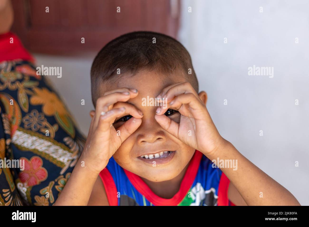 A young Thai boy puts his fingers around his eyes like binoculars making a funny face Stock Photo