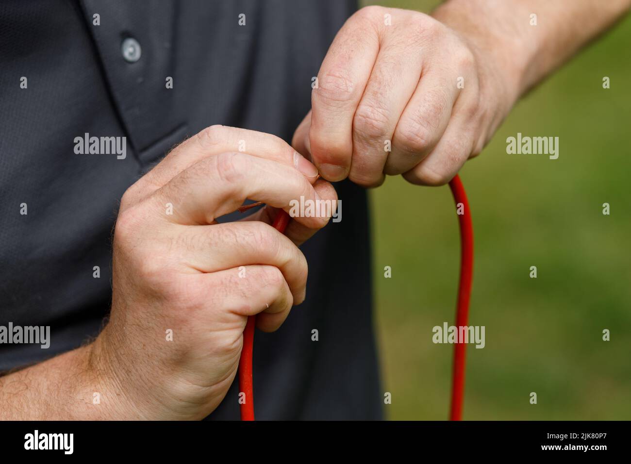Hands connecting electrical wires together. Male hands and fingers holding a severed red wire Stock Photo