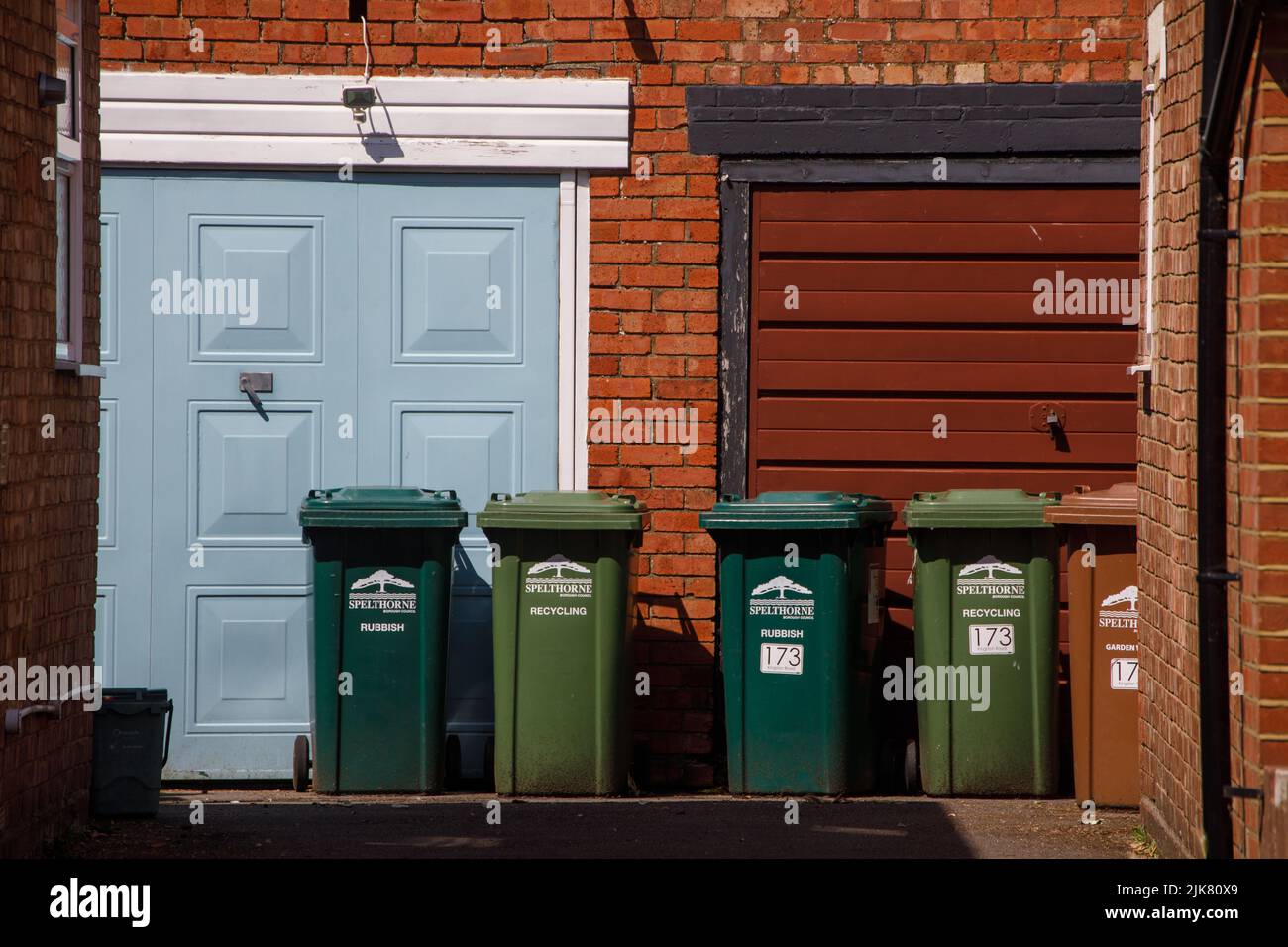Green garbage wheelie bins outside two garage doors on a shared drive