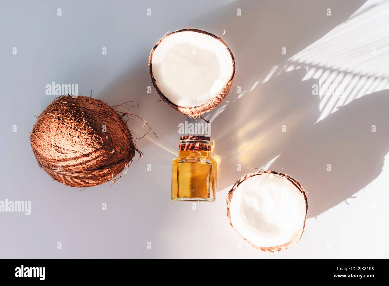 Coconut oil and fresh coconuts on white background in palm leaf shadow