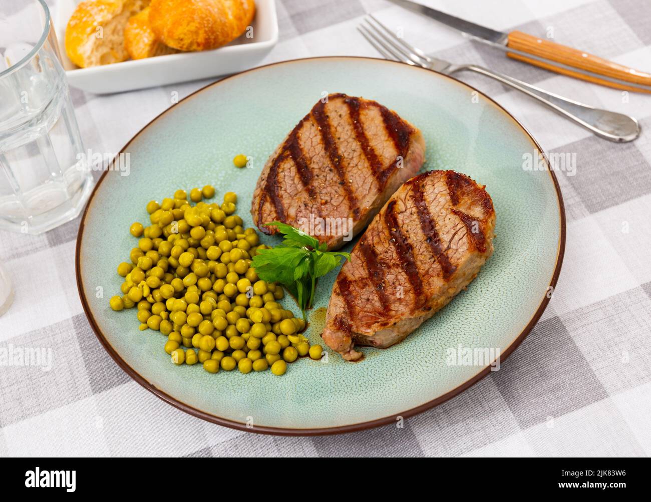 Two grilled veal steaks with canned green peas and parsley Stock Photo