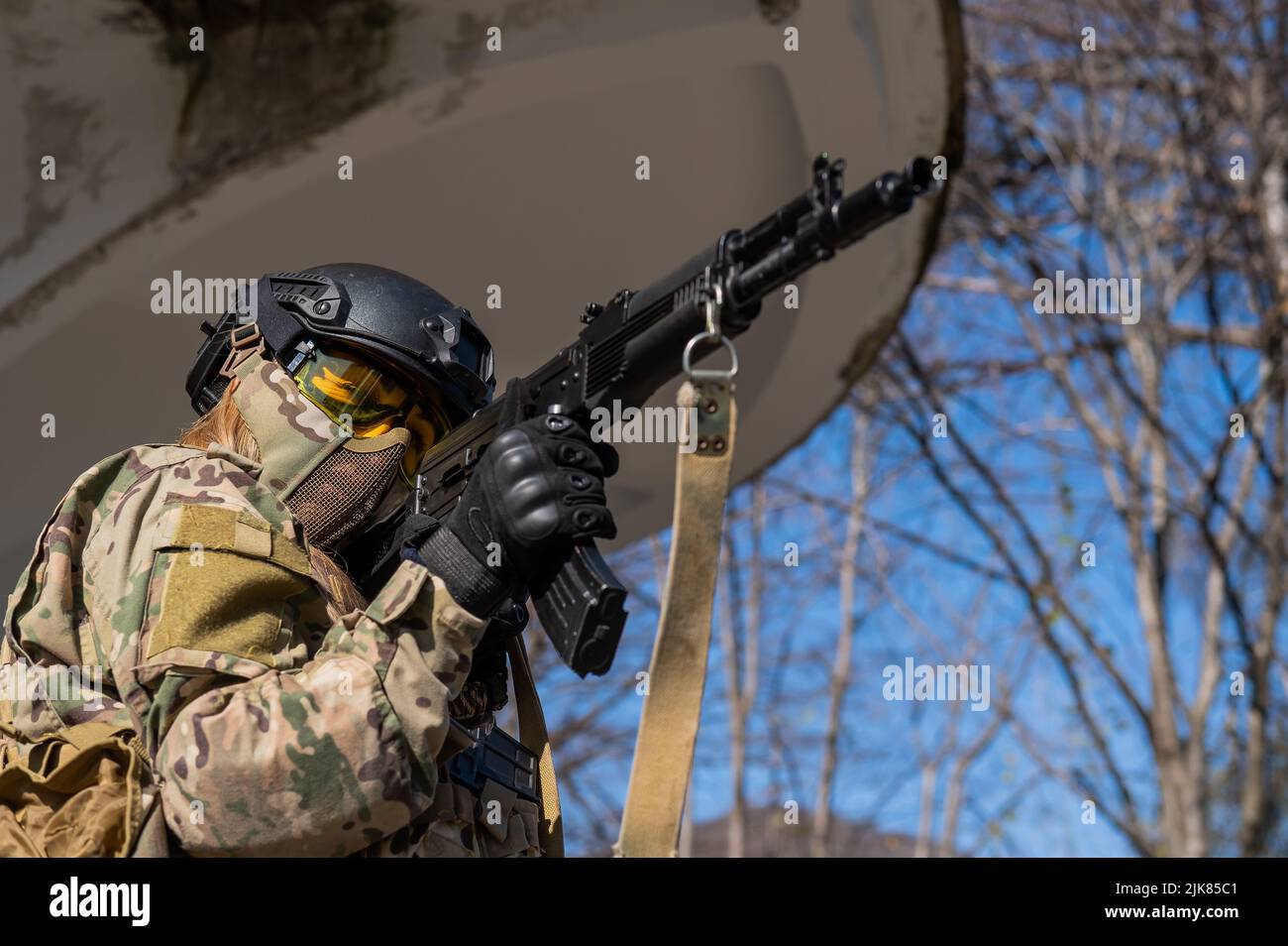 Portrait of a woman in a helmet and goggles with a machine gun in her ...