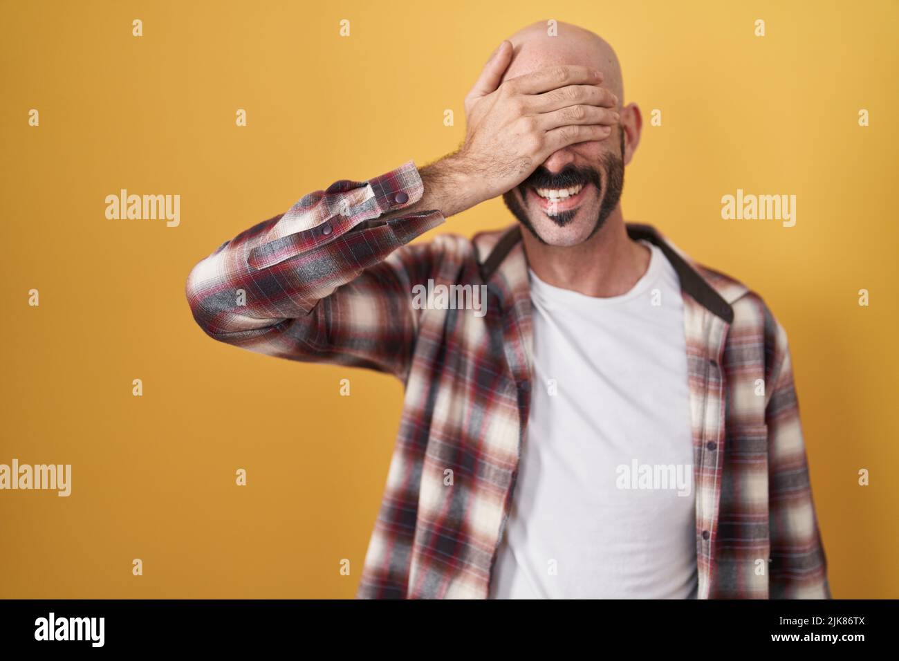 Hispanic man with beard standing over yellow background smiling and