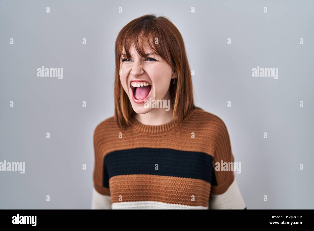Young beautiful woman wearing striped sweater over isolated background ...