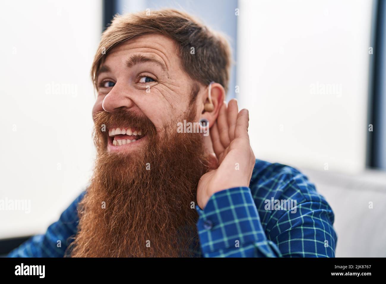 Young redhead man using deafness aid machine sitting on sofa at home Stock Photo