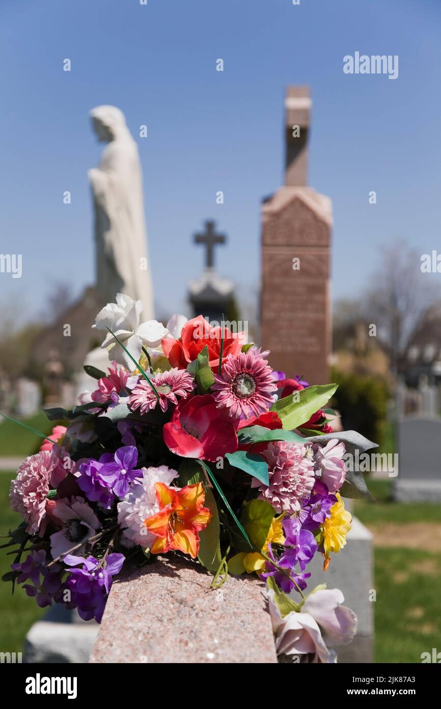 Close-up of a bouquet of artificial flowers atop a headstone in a cemetery. Stock Photo