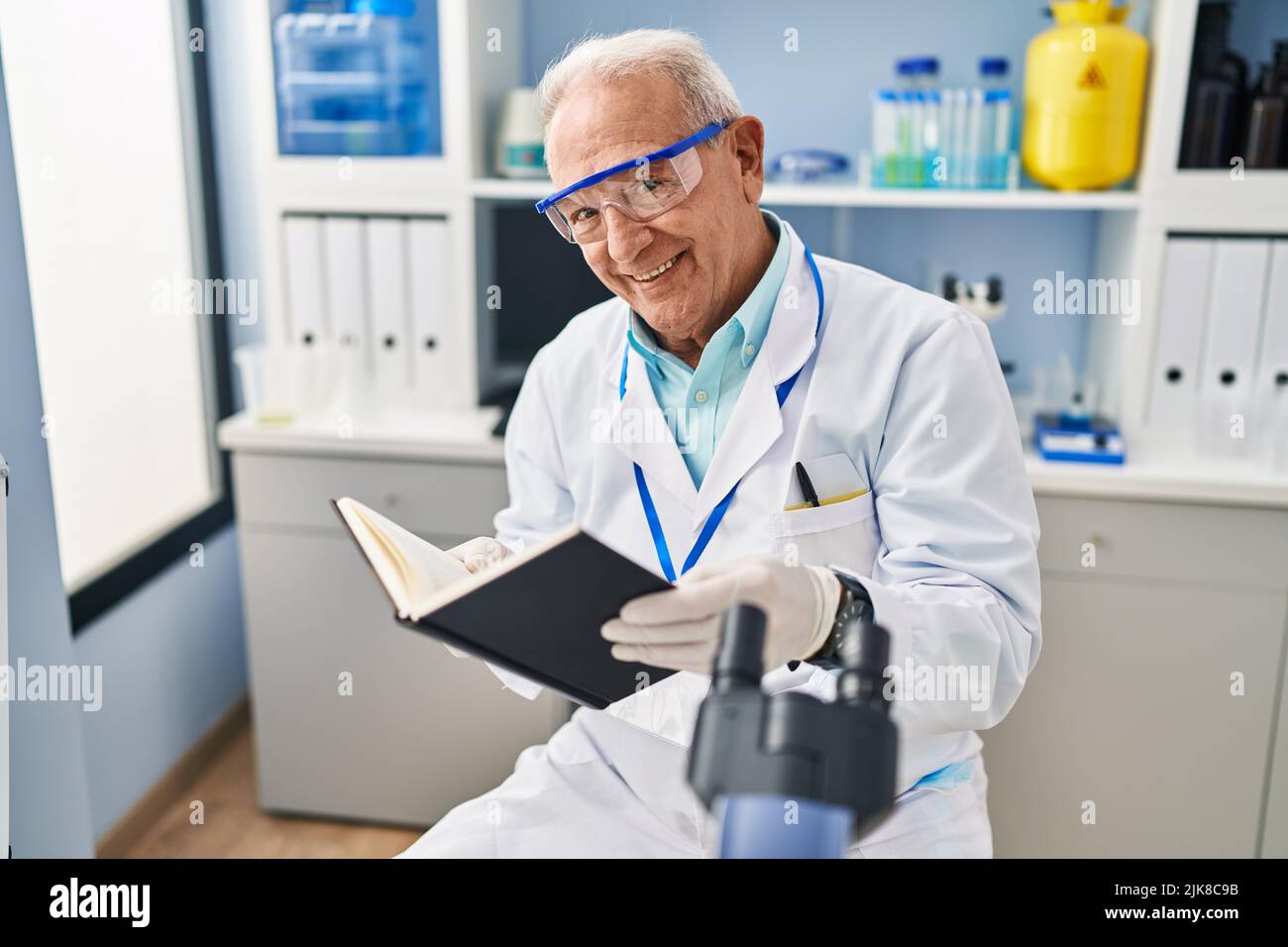 Senior man wearing scientist uniform reading book at laboratory Stock ...