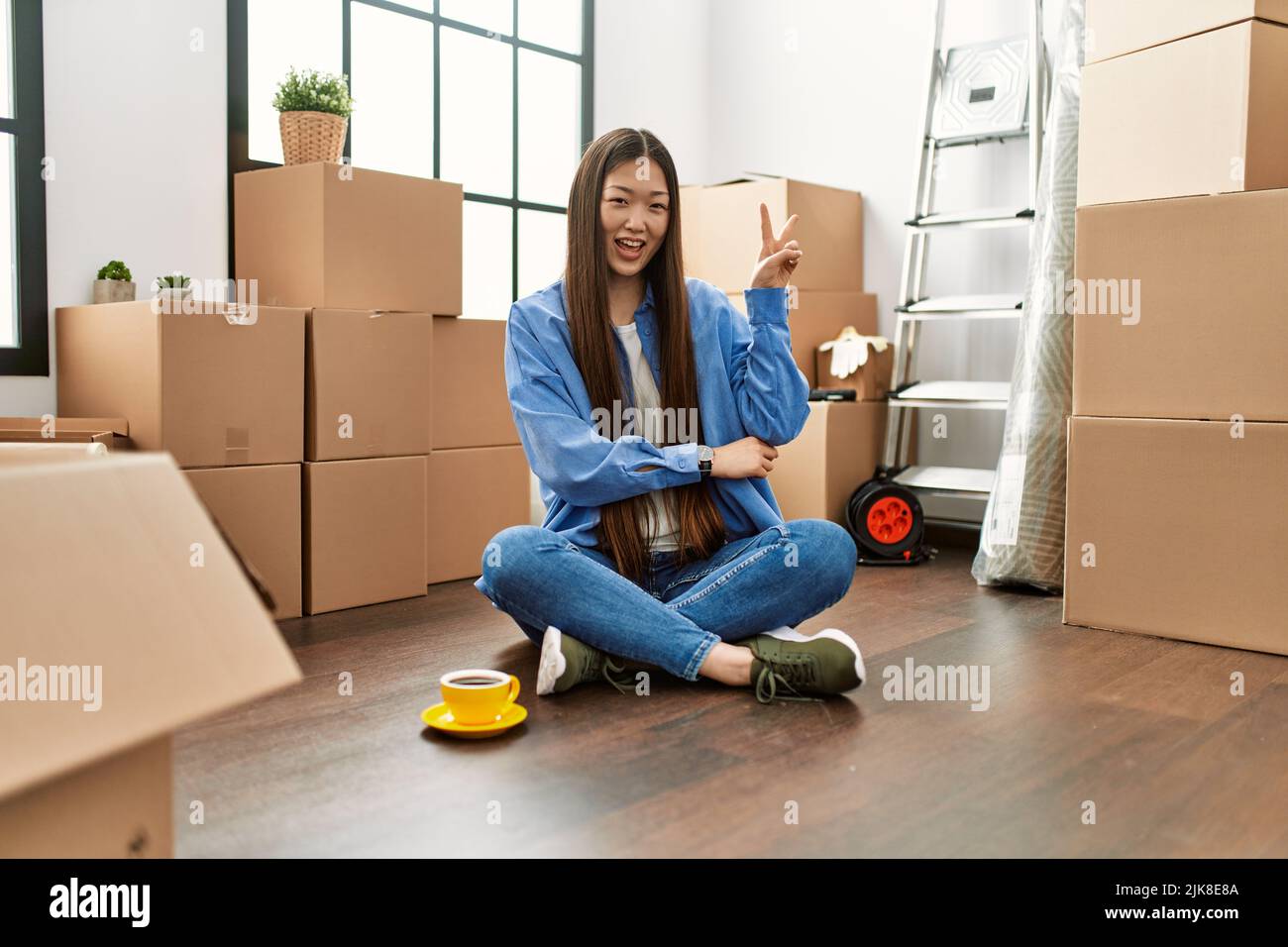 Young chinese girl sitting on the floor at new home smiling with happy ...