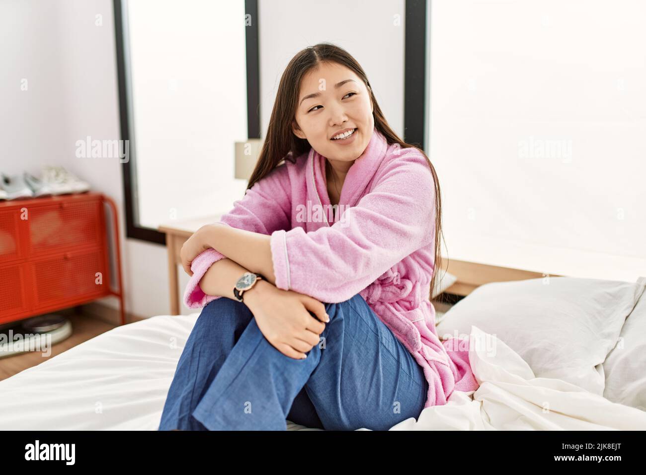 Young chinese girl smiling happy sitting on the bed at bedroom Stock ...