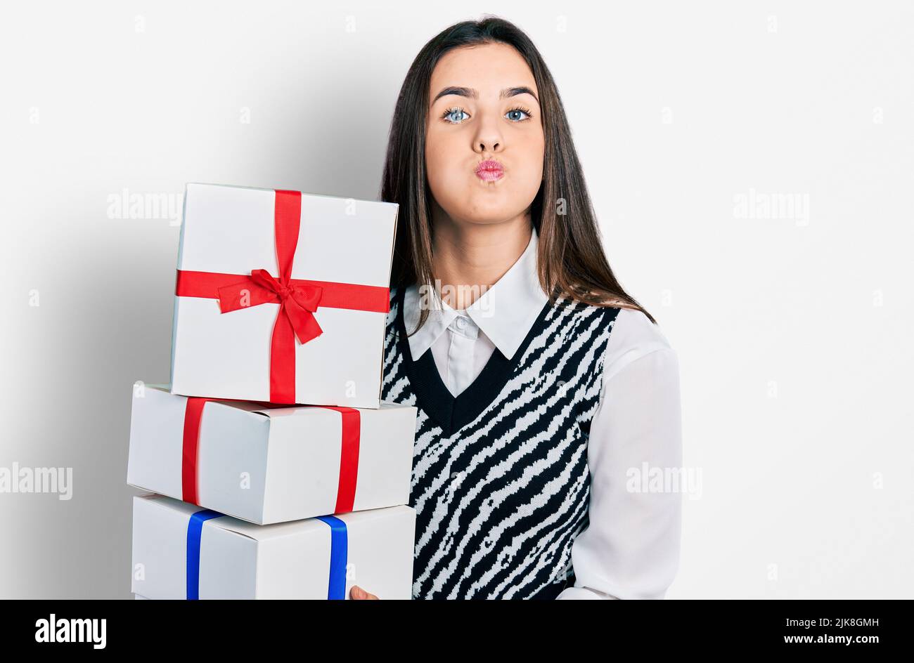 Young brunette teenager holding gifts puffing cheeks with funny face. mouth inflated with air, catching air. Stock Photo