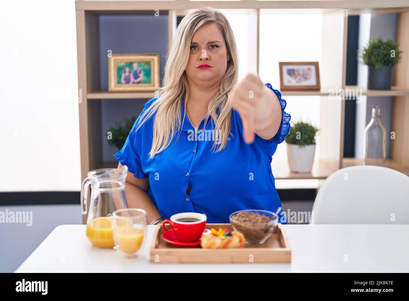 Caucasian plus size woman eating breakfast at home looking unhappy and ...