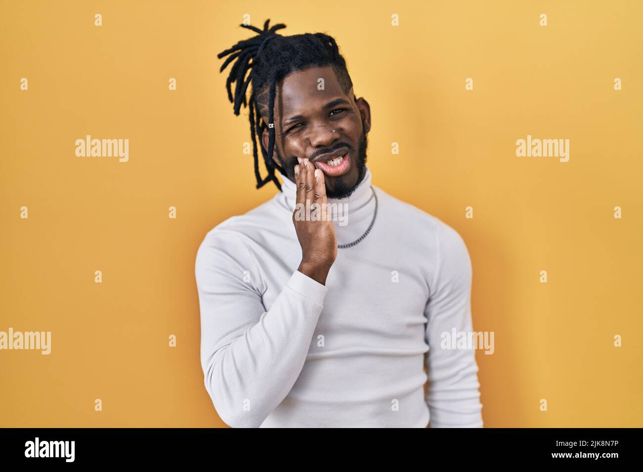 African man with dreadlocks wearing turtleneck sweater over yellow