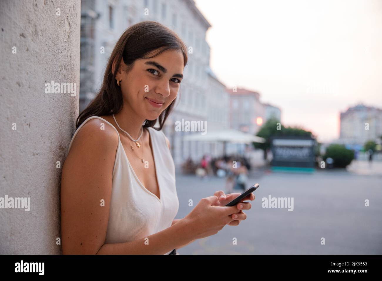 Young girl in town leaning against a pole messages with her cell phone. Stock Photo
