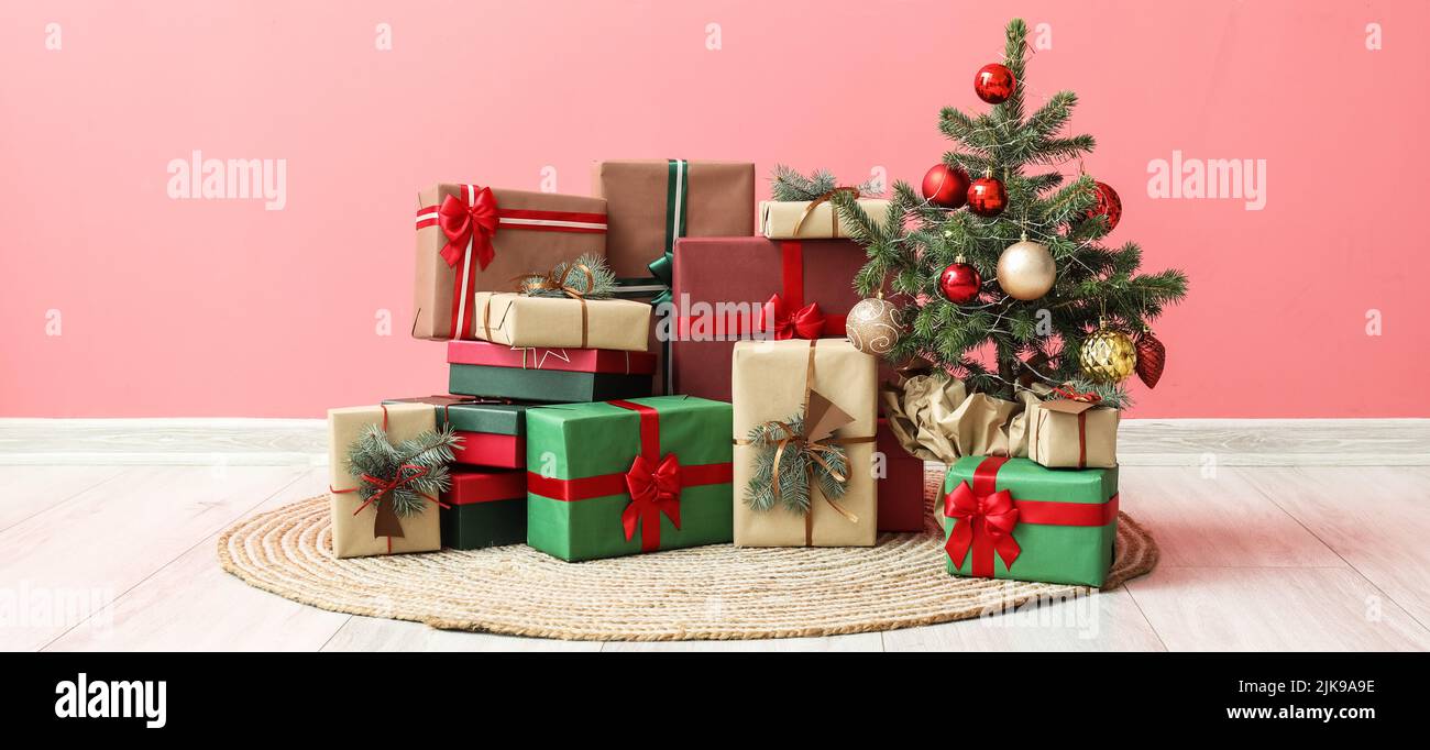 Heap of Christmas gift boxes with fir tree near pink wall in room Stock