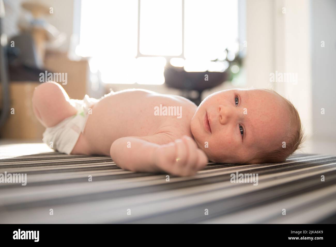A little cute baby in a diaper restlessly lying on his back on striped