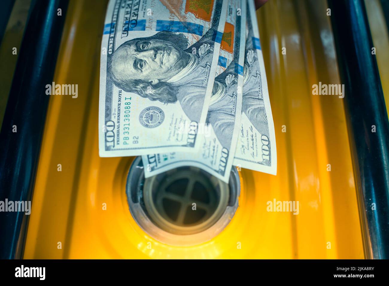 A closeup of a one hundred dollar bill in a fuel filler neck in a