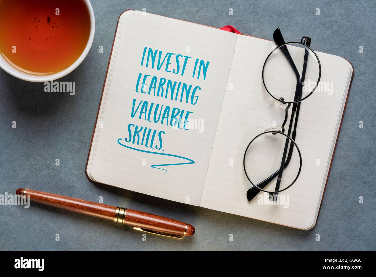 invest in learning valuable skills - inspirational advice, writing in a notebook, flat lay with tea, education and personal development concept Stock Photo