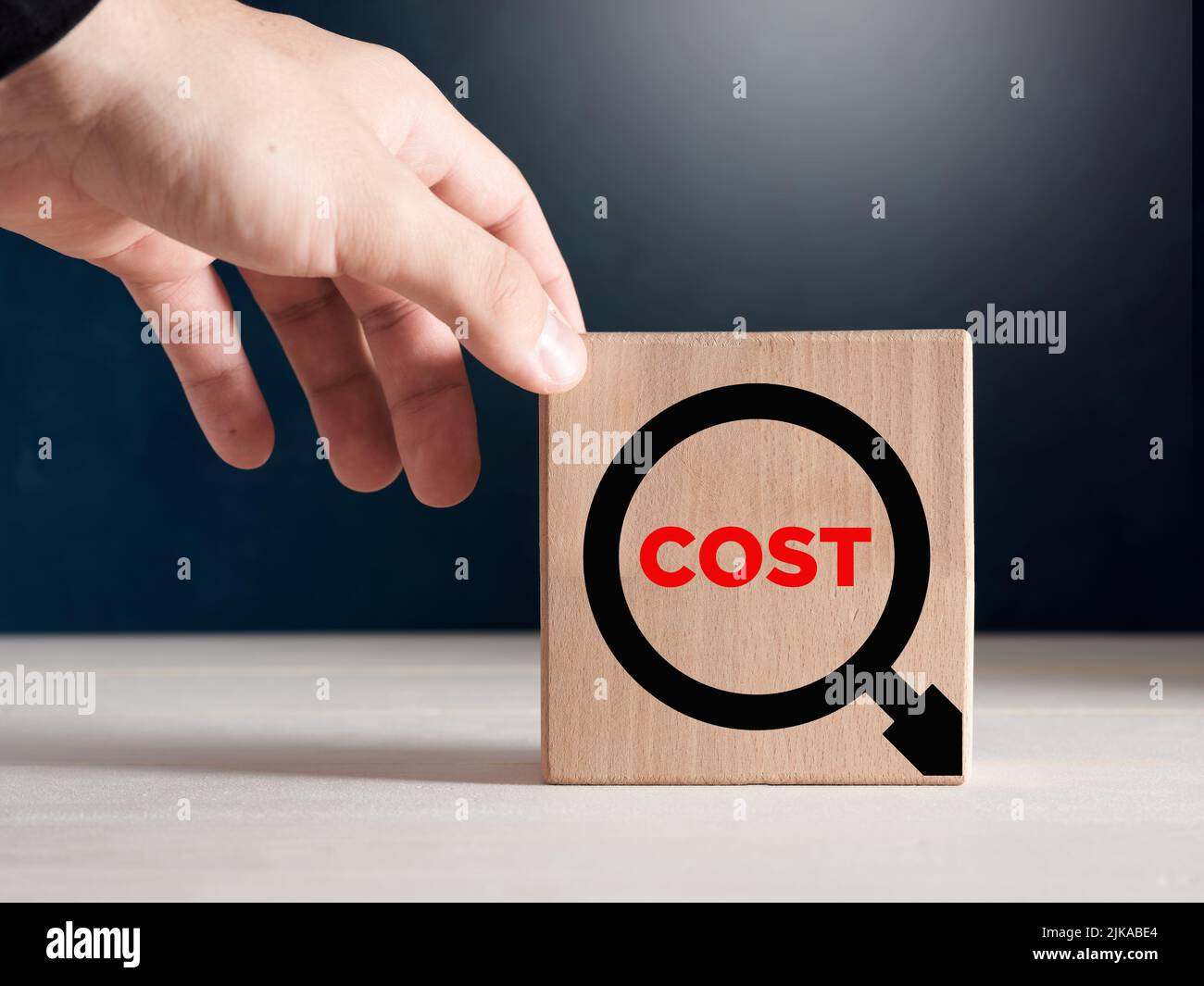 Male hand places the wooden cubes with the word cost with a magnifying glass icon. Cost analysis concept. Stock Photo