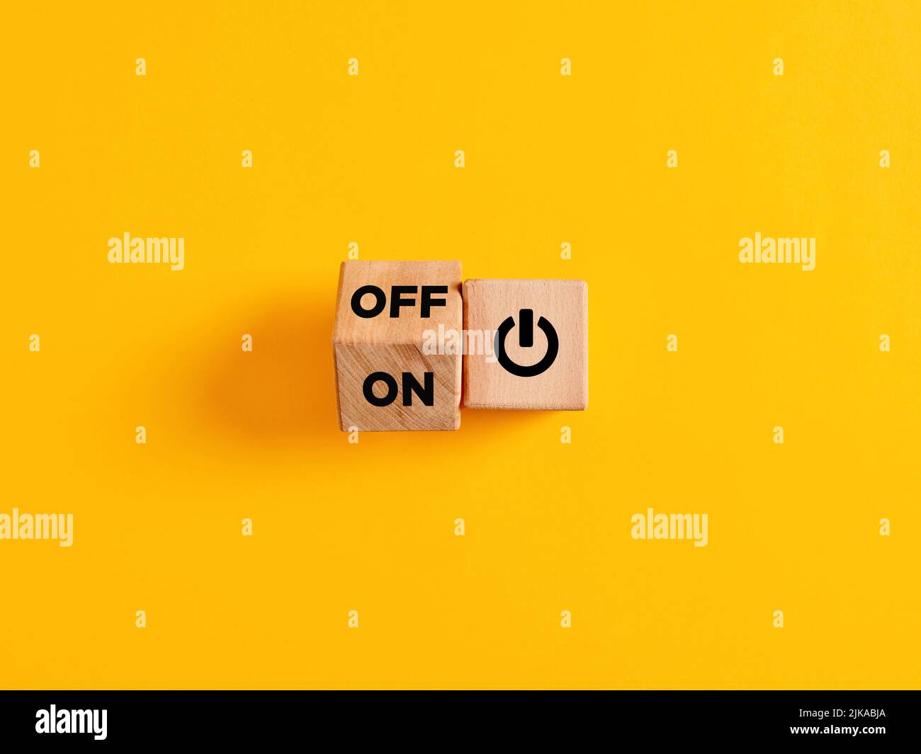 The words on and off on wooden cubes with start icon on yellow background. Power on off switch or start and stop button concept. Stock Photo