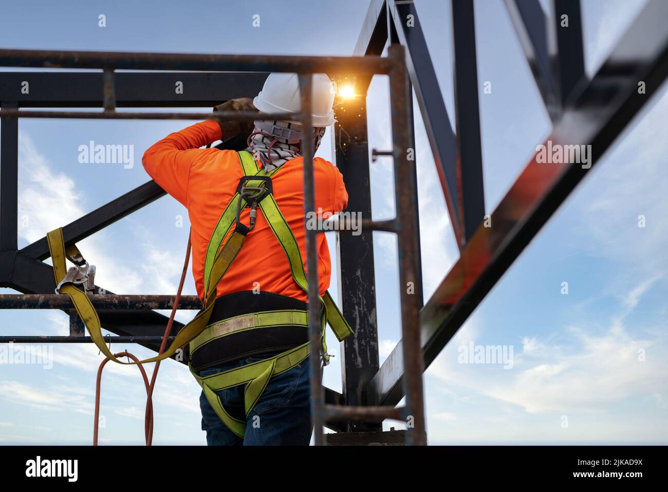 Industrial steel roof truss welders wear safety clothing on the construction site. Fall arrestor device for worker with hooks for safety body harness. Stock Photo