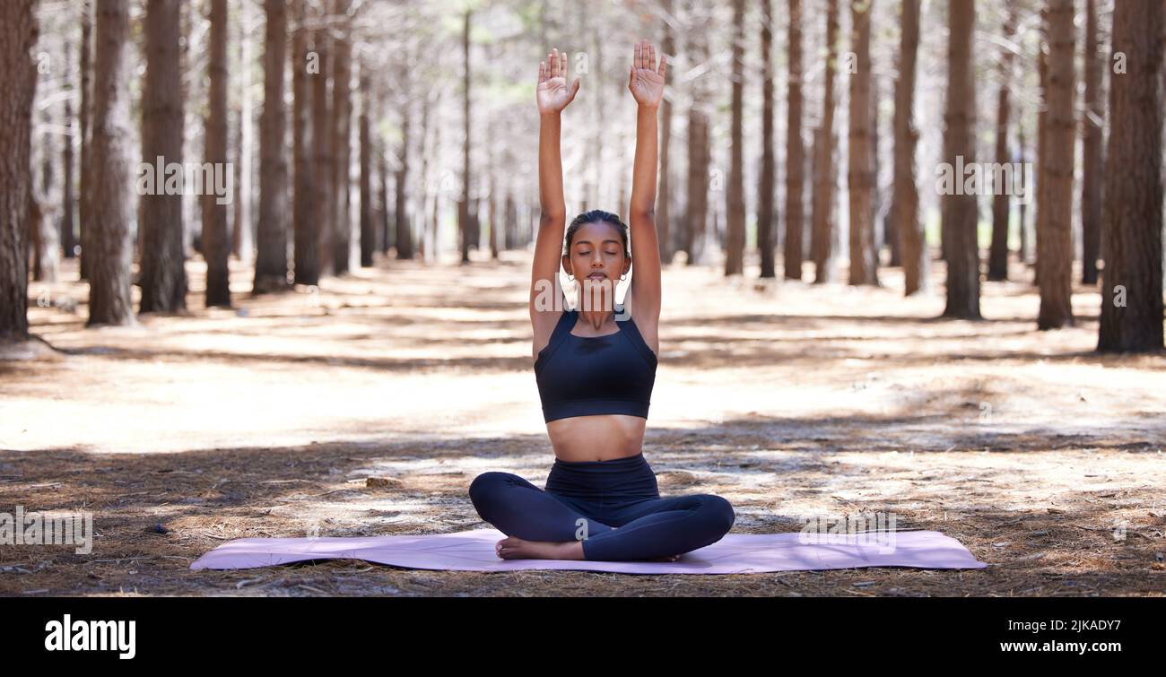 Releasing all that no longer serves me. an attractive young woman sitting alone on a yoga mat outdoors and meditating. Stock Photo
