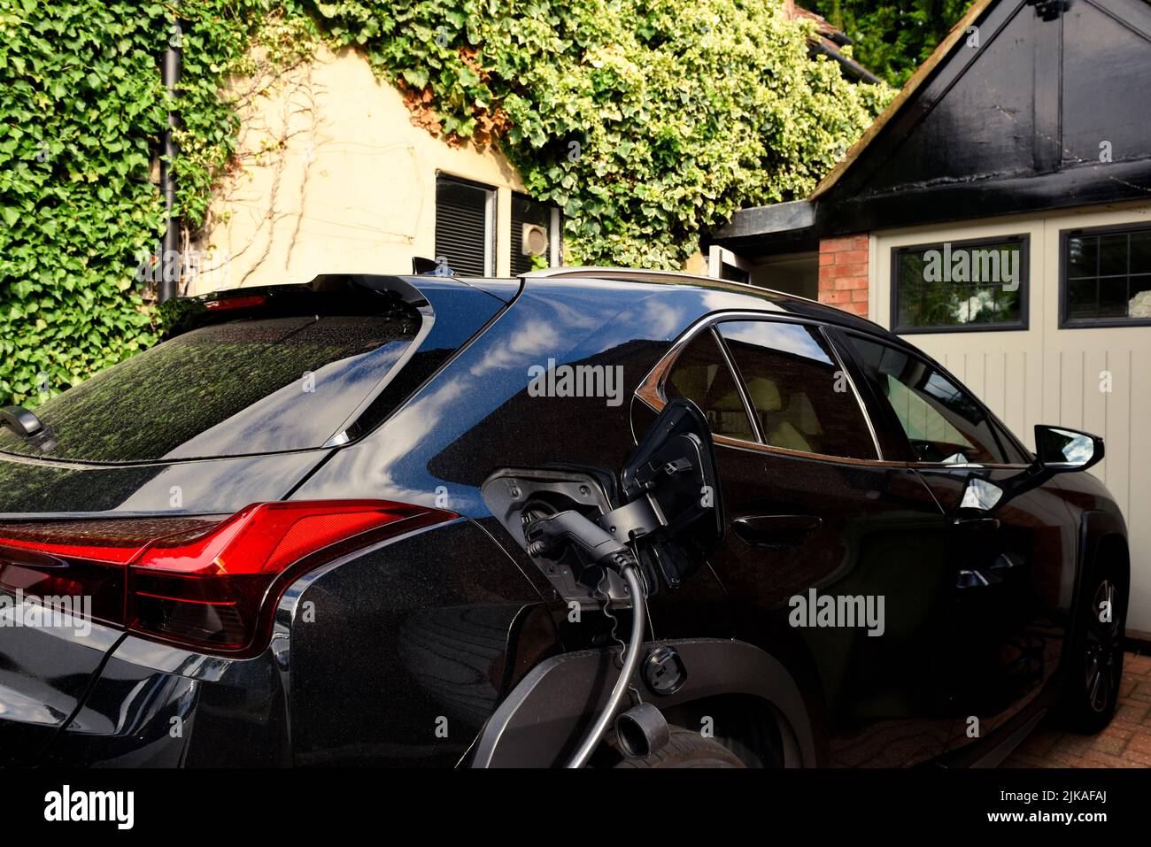 Electric car plugged in to charge outside home with power cable Stock Photo