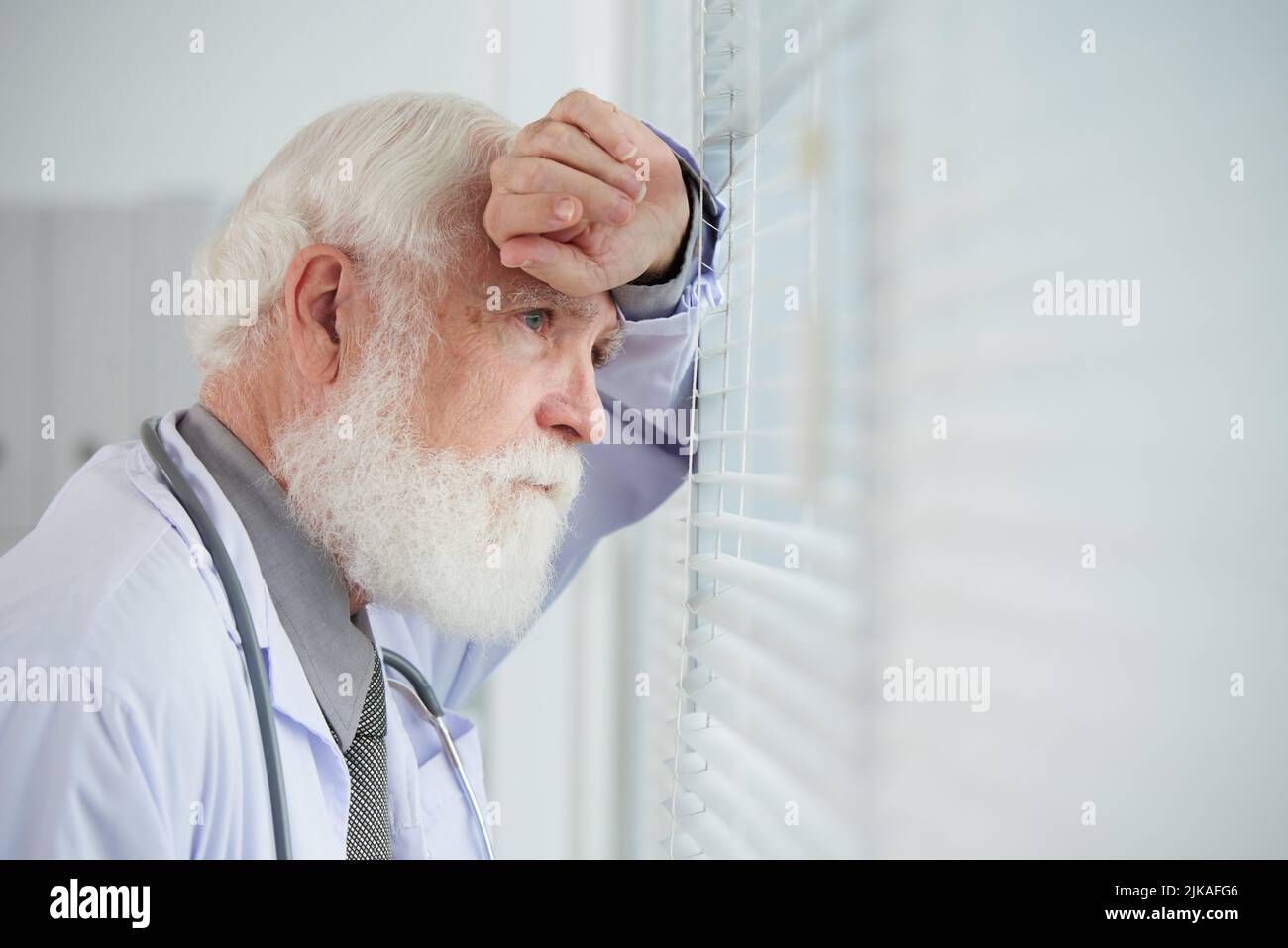 Thoughtful aged general practitioner looking through window in his office Stock Photo