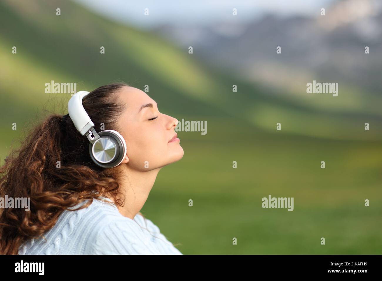 Side view portrait of a woman wearing wireless headphones relaxing listening audio in the mountain Stock Photo