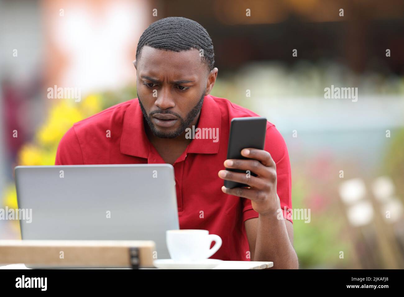 Worried black man in red using multiple devices in a bar terrace Stock Photo