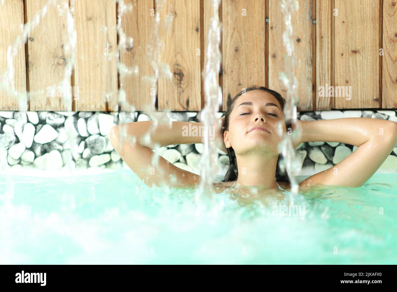 Front view portrait of a woman relaxing with arms on head under water jet in a spa Stock Photo