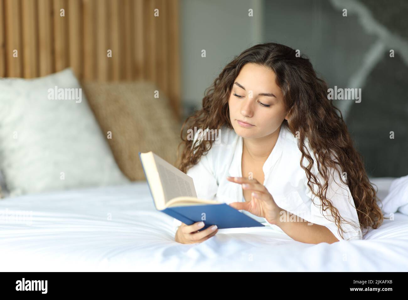Concentrated woman on a hotel bed reading a paper book Stock Photo
