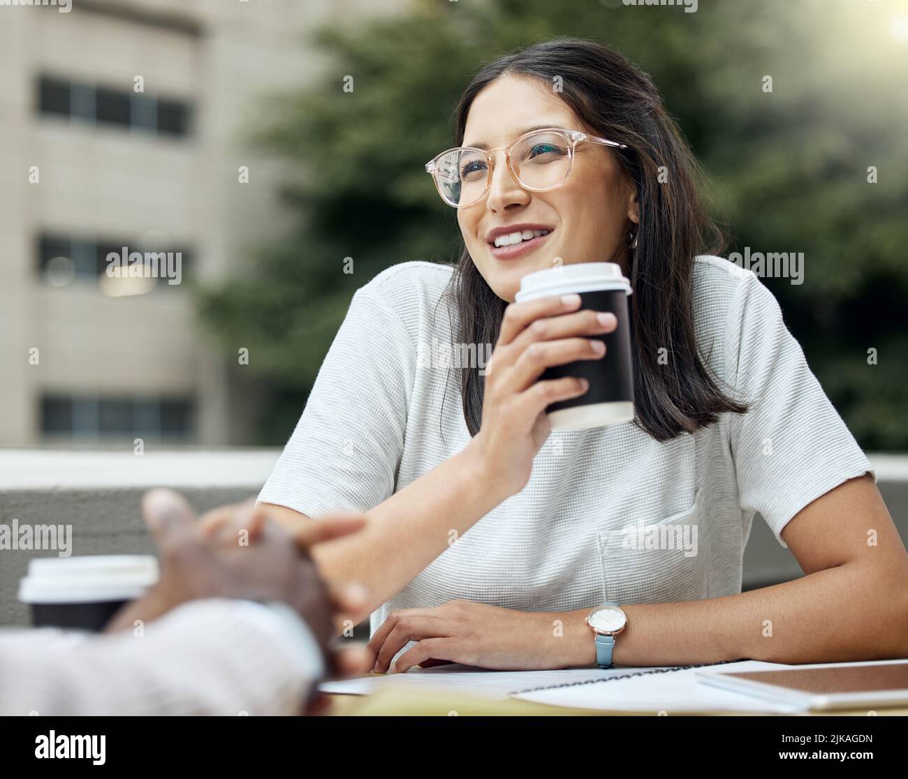 Sharing some light-hearted exchanges with her colleagues over coffee. a young businesswoman having a break with her colleagues outside an office. Stock Photo
