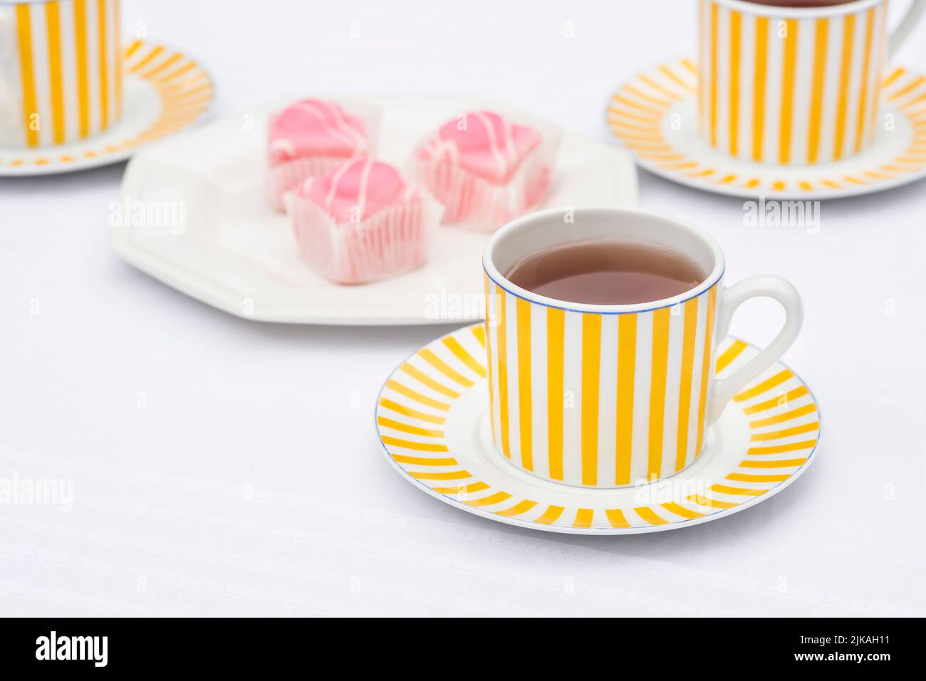 Food / teatime treat: Close up of pink fondant icing covered sponge cakes and black tea. Stock Photo