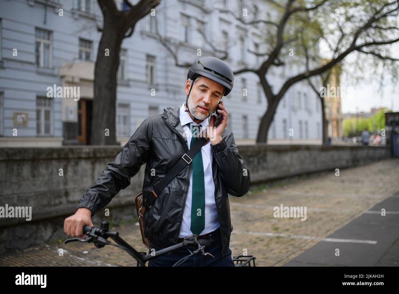 Portrait of businessman commuter on the way to work, pushing bike and calling on mobile phone, sustainable lifestyle concept. Stock Photo