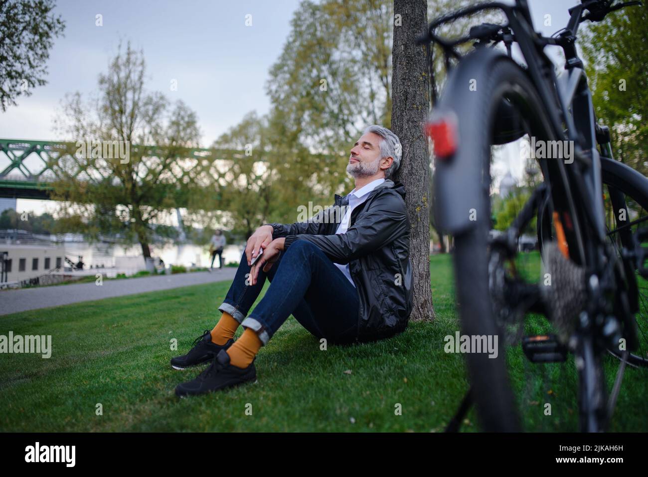 Businessman with bike sitting on grass in park, enjoying leisure time. Commuting and alternative transport concept. Stock Photo