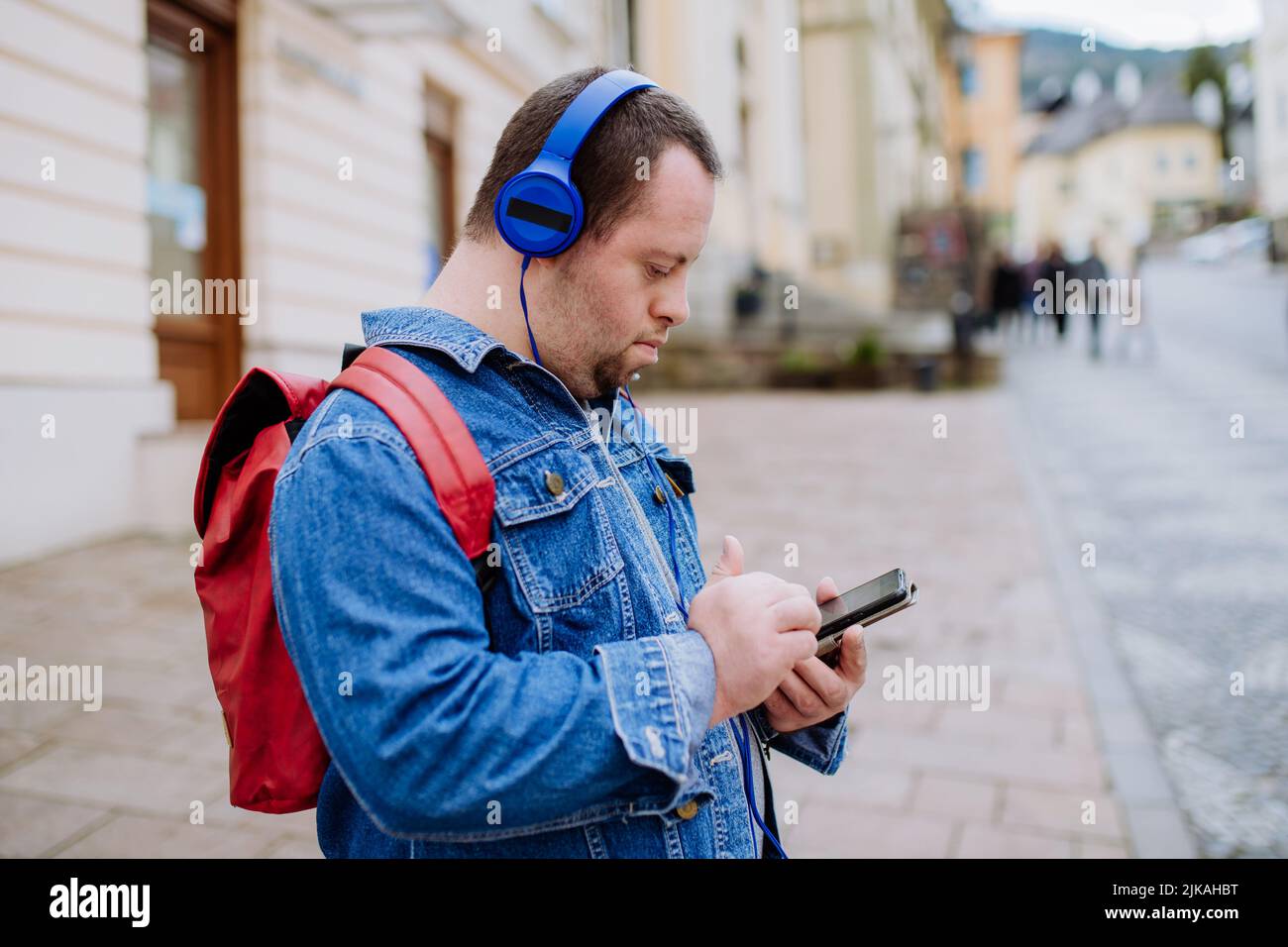 Happy young man with Down sydrome listening to music when walking in street. Stock Photo