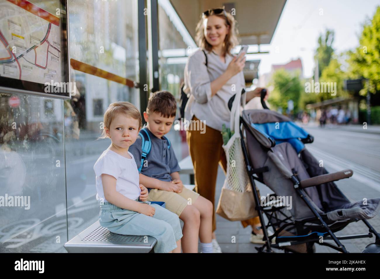 Young mother with little kids waiting on bus stop in city. Stock Photo