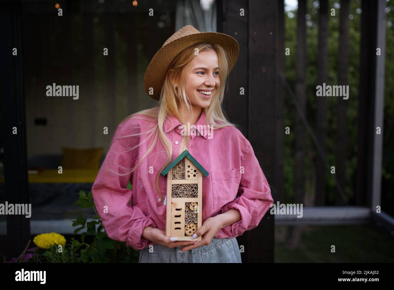 Young woman garedener holding bug and insect hotel on terrace in garden, sustainable lifestyle. Stock Photo